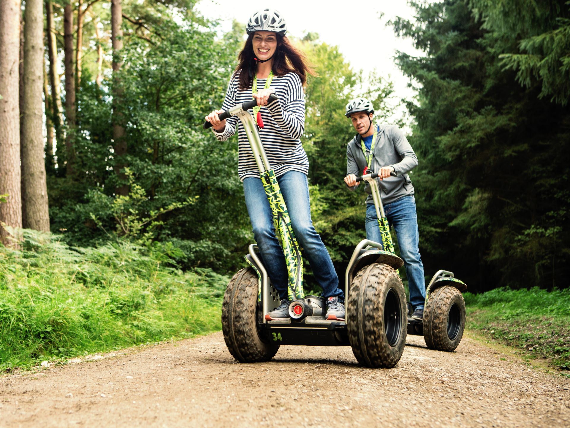 a woman followed by a man both with big smiles whilst riding Go Ape Forest Segways