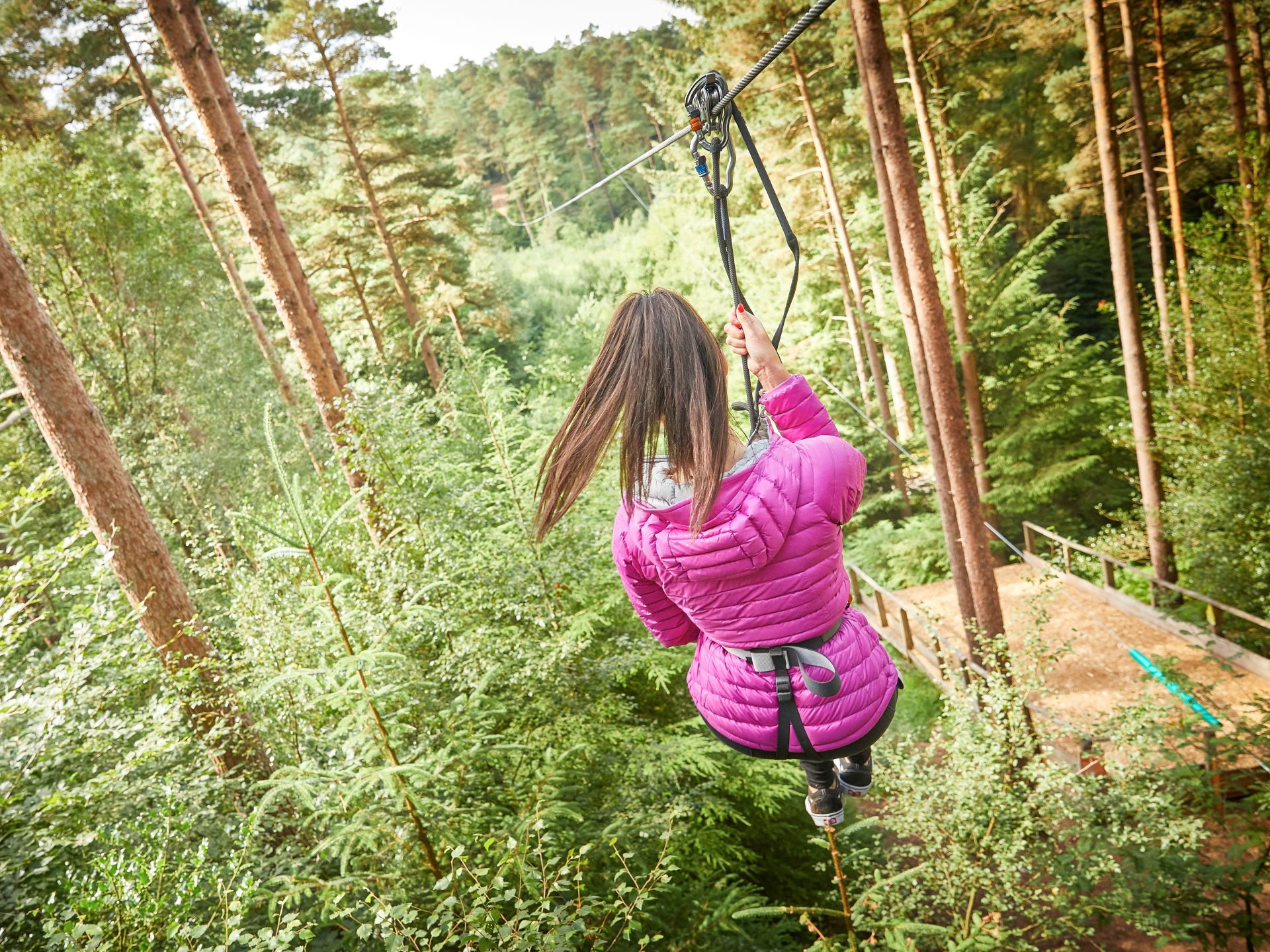 a woman wearing a pink jacket riding a Go Ape zip wire in the forest