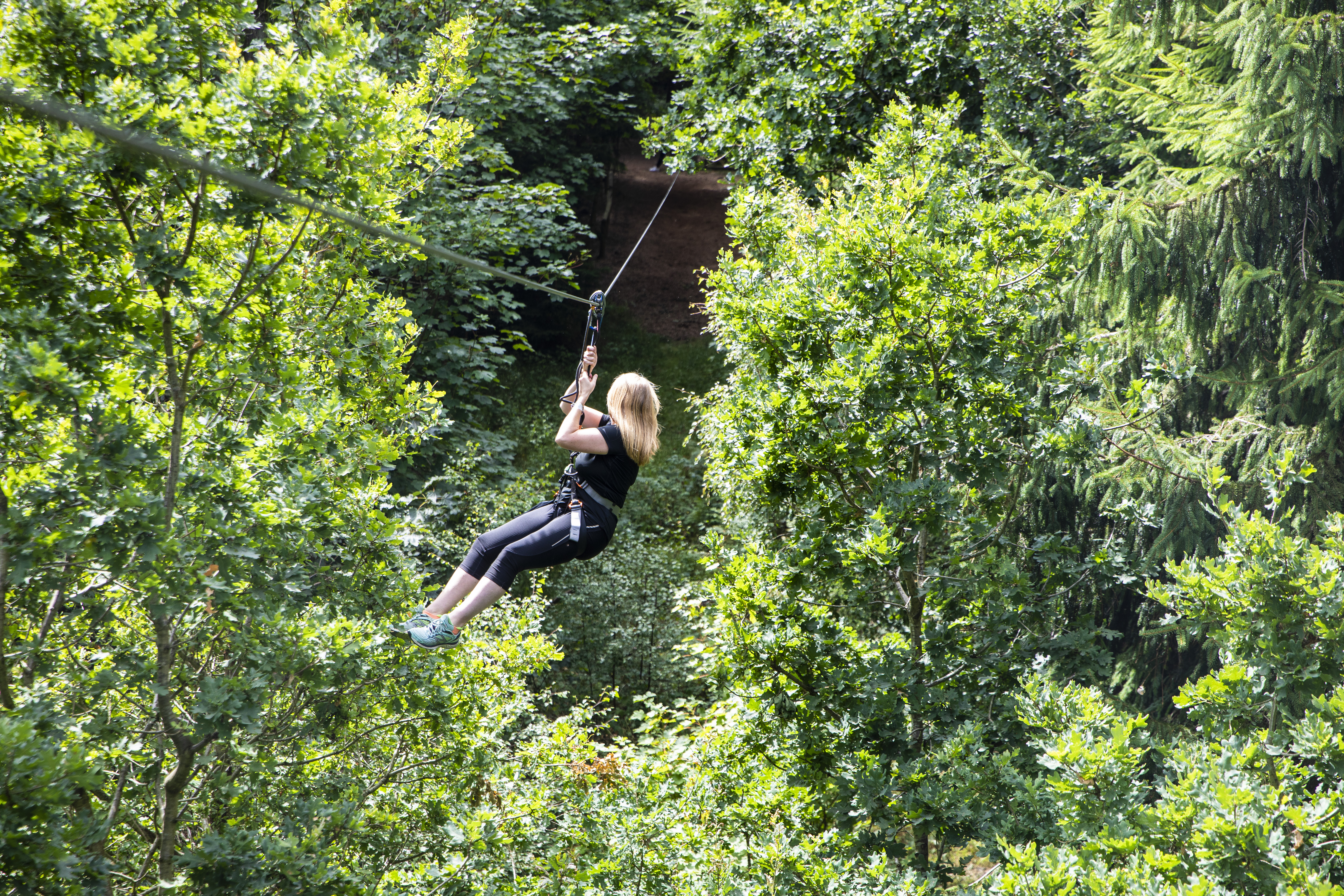 woman in black t-shirt flying down a zip line on a Go Ape Treetop Challenge adventure 