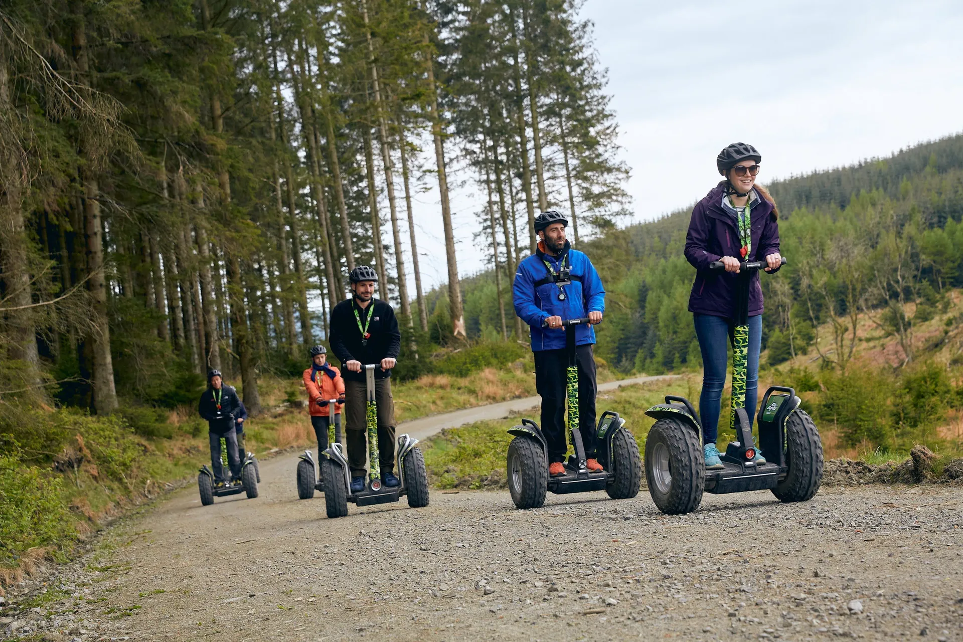 A group rides on Segways on a trail next to trees.
