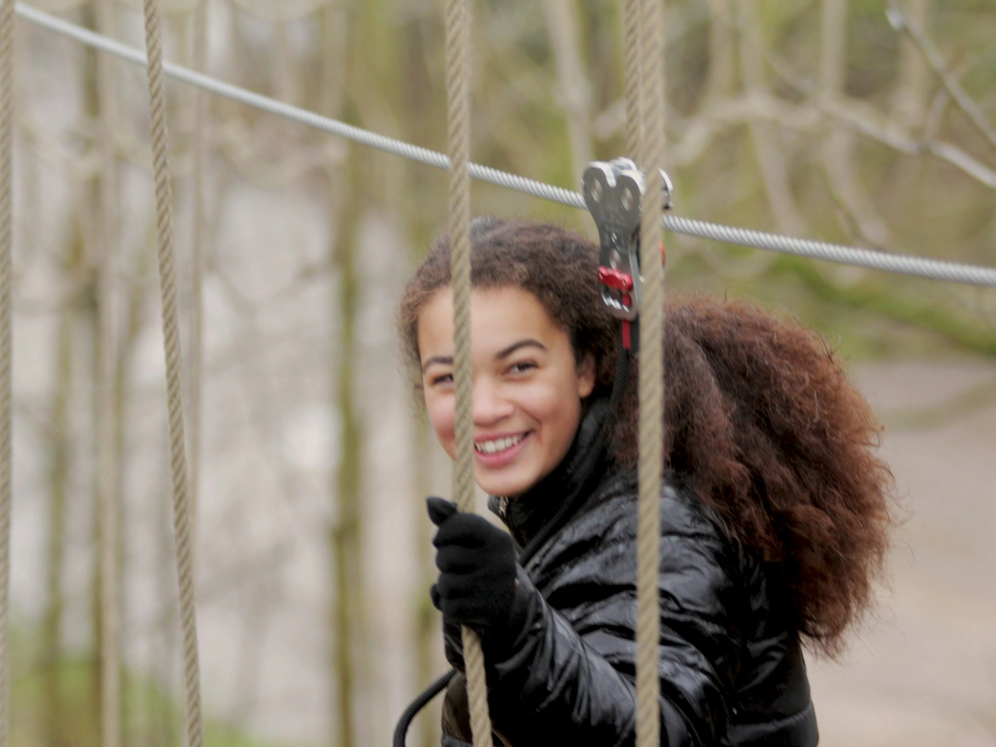Young person smiles while crossing a high ropes course.