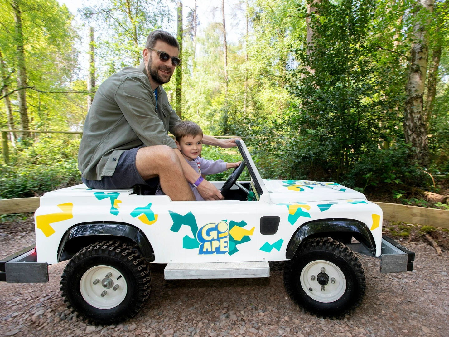 Adult and young person in a Mini Land Rover on a track in the forest.