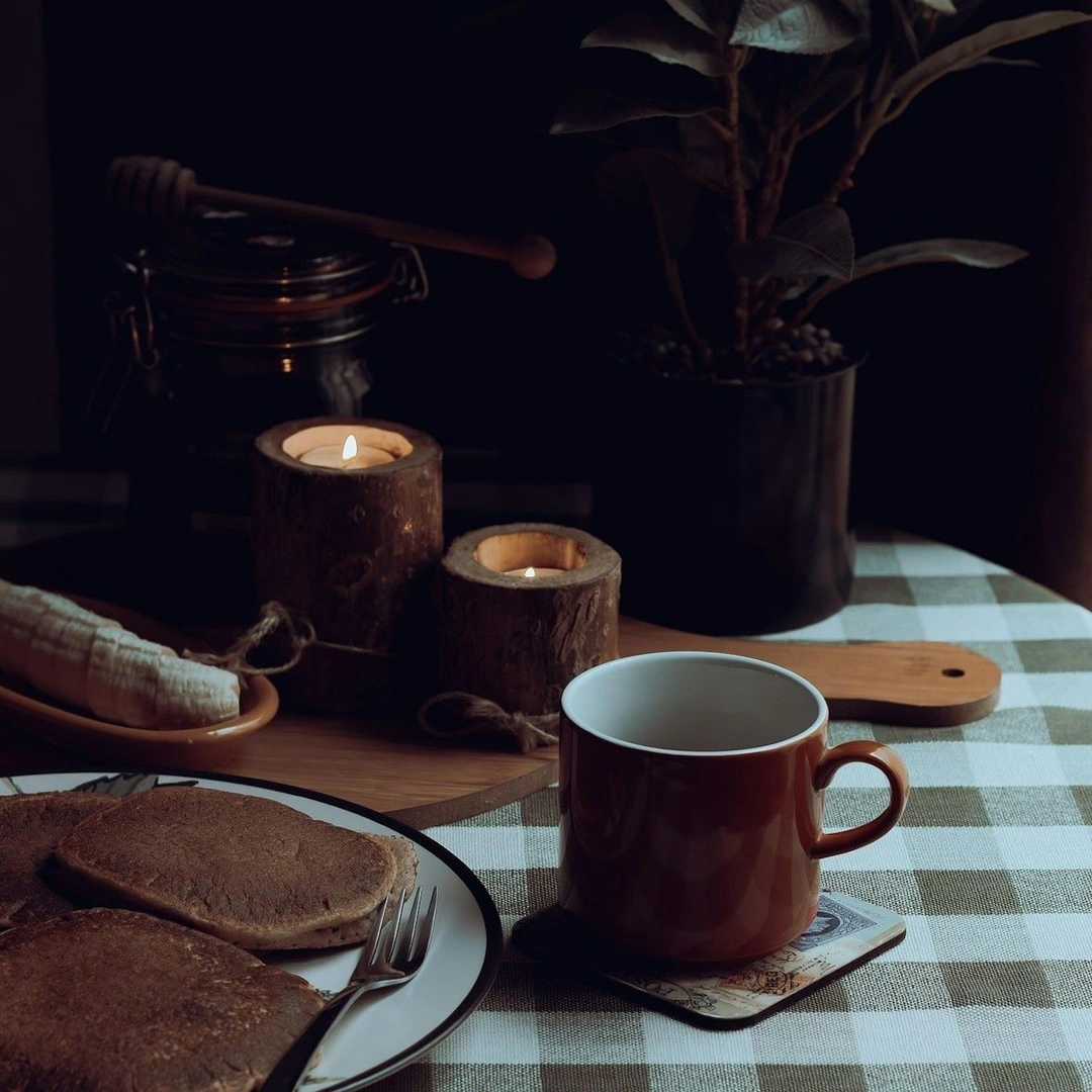 A coffee cup and a plate of pancakes sit on a table in a rustic cafe