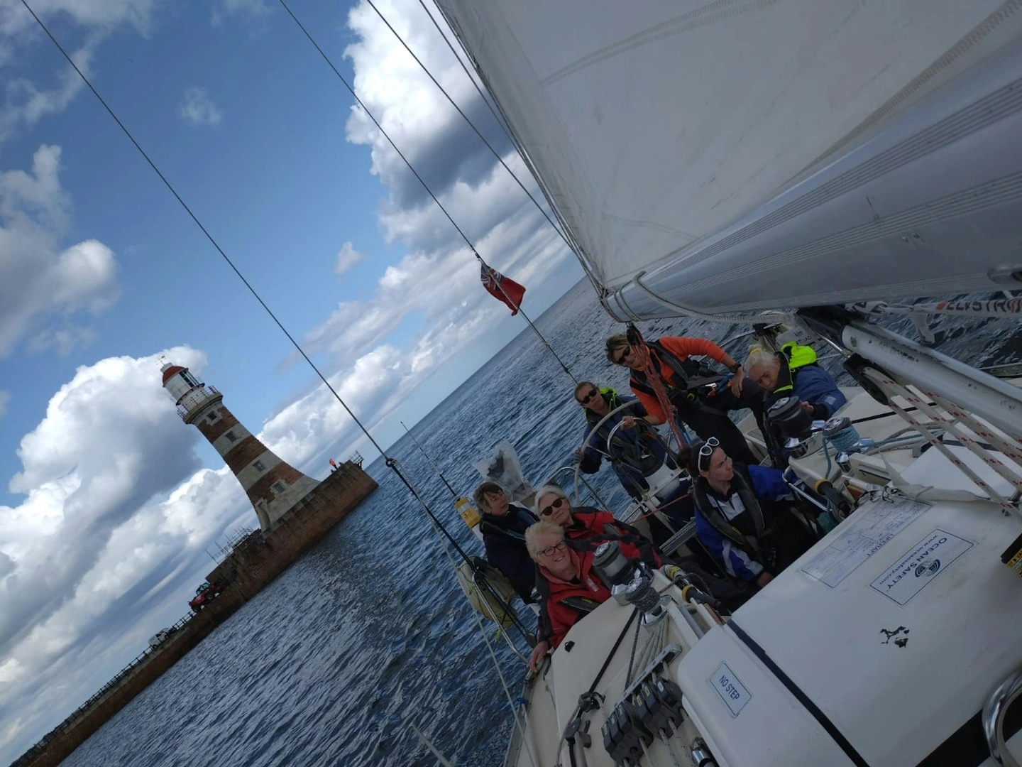 A group on a sailing boat with a lighthouse behind them.