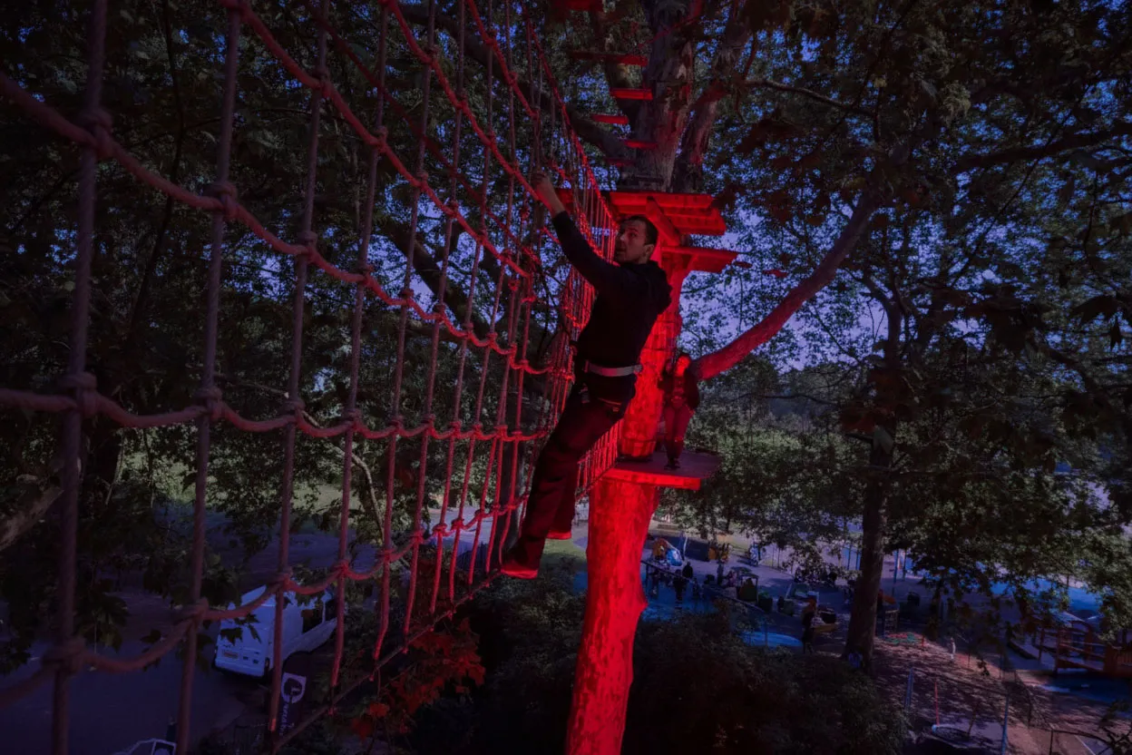 A man takes on a Go Ape high ropes cargo net whilst his partner watches on from a platform behind