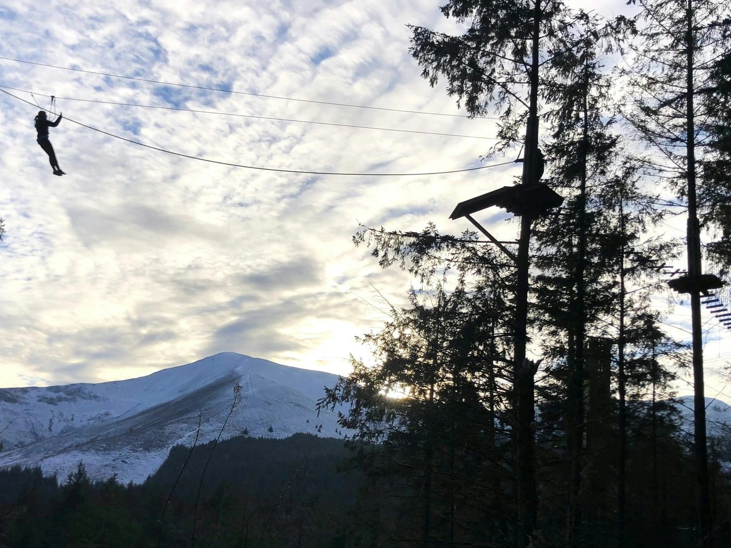 Silhouette of a person on a zipline with mountain scenery in the background.