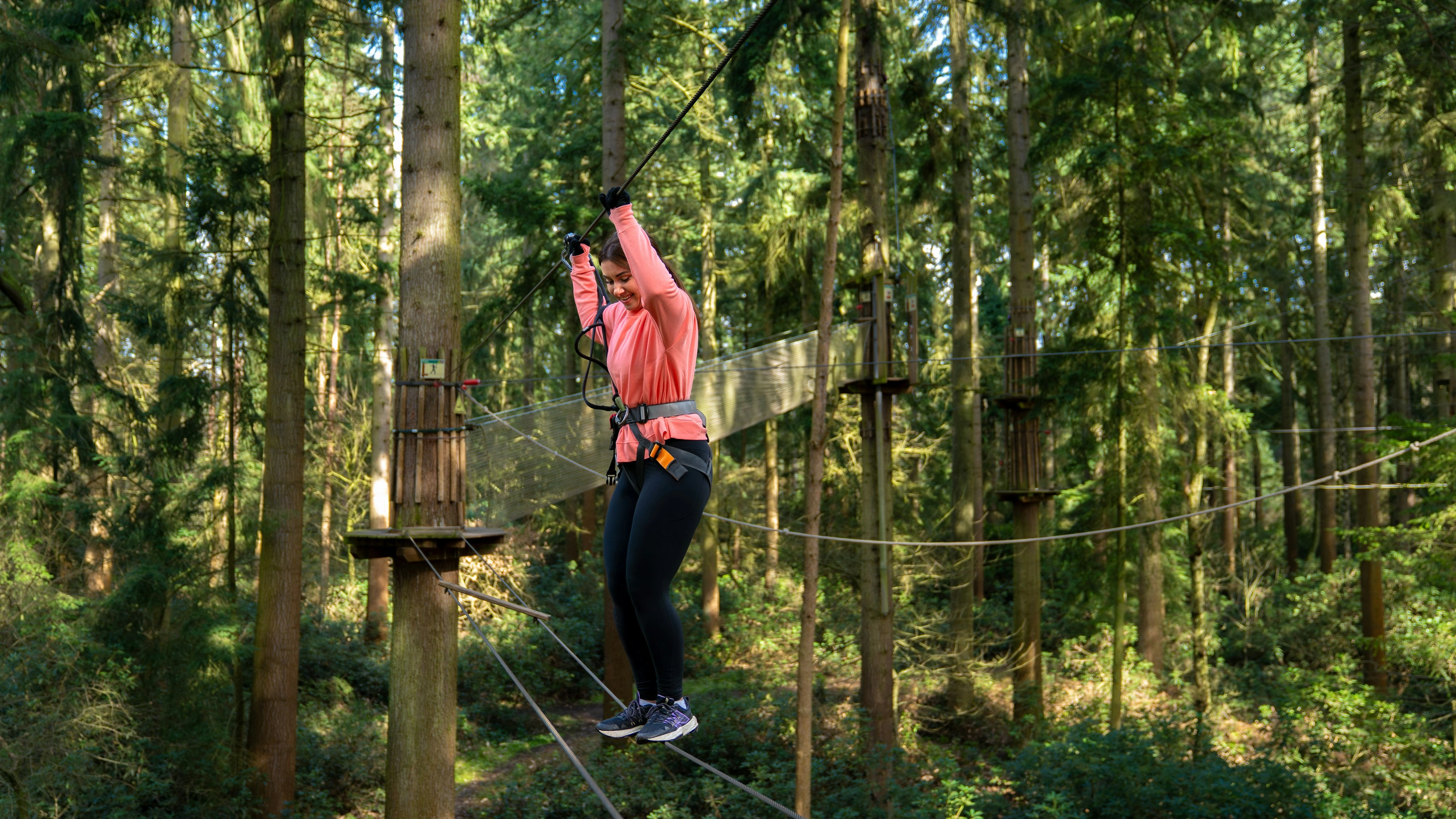A woman shuffles her way over a high ropes crossing on a forest adventure