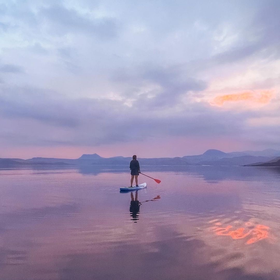 a person riding a paddleboard on calm coastal waters in Scotland