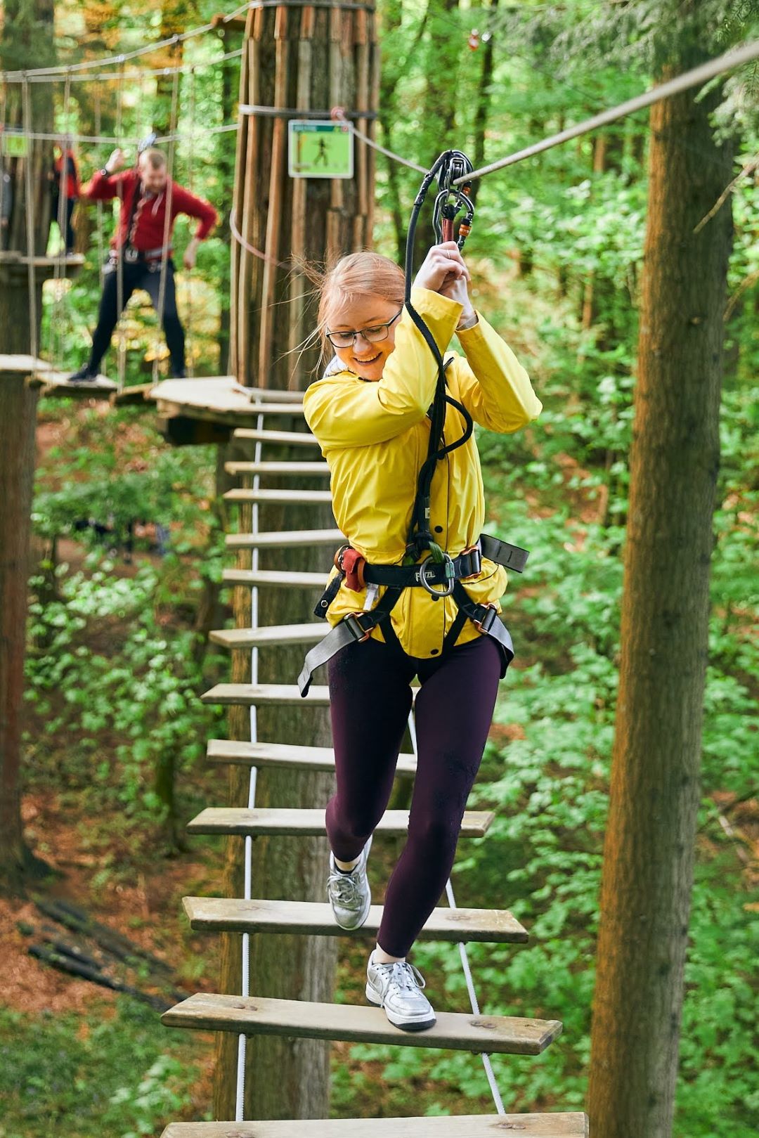 A student smiles as she balances across a Go Ape obstacle in the treeops