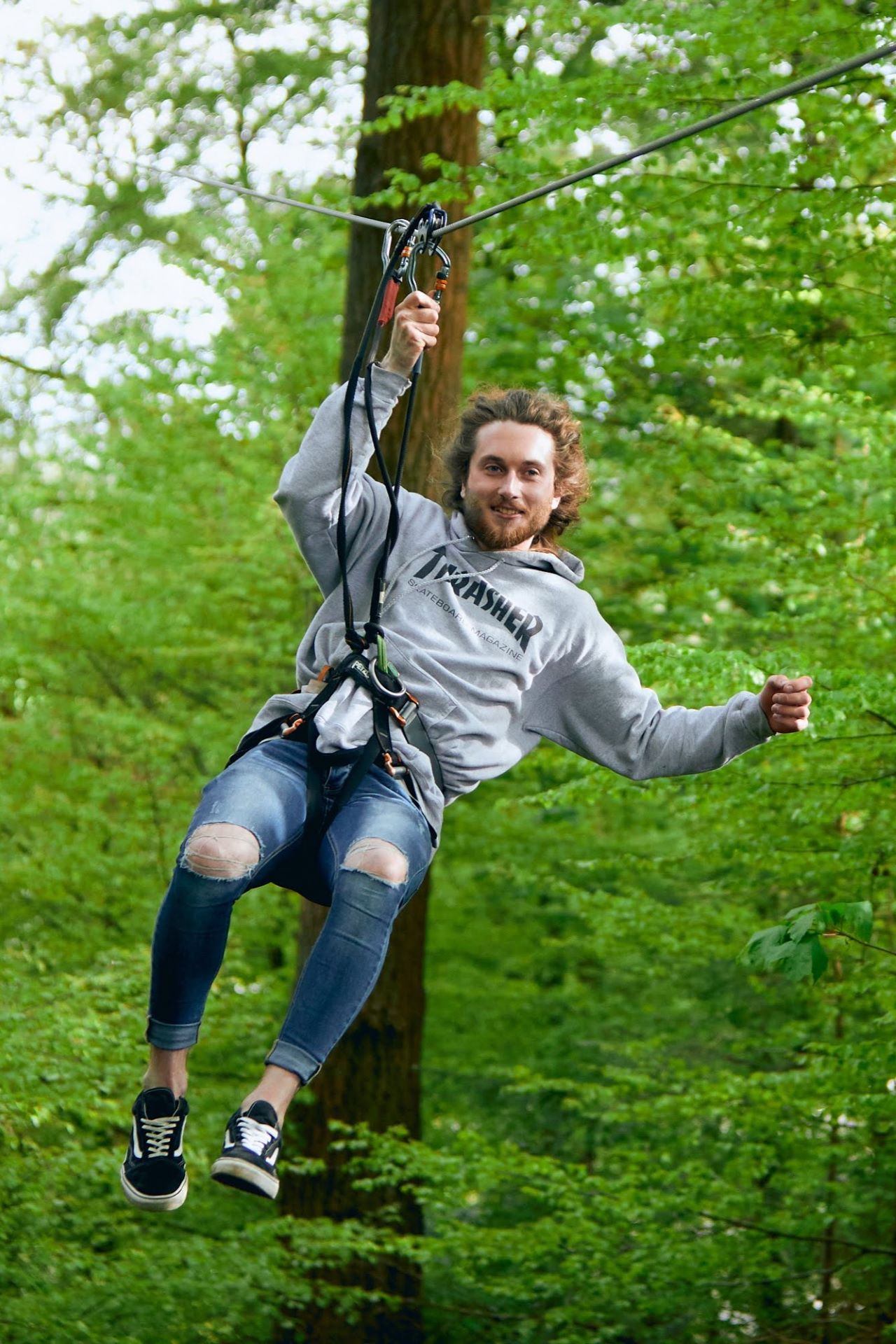 A student wearing a grey hoodie glides down a Go Ape zip wire in the forest.