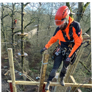 A Go Ape construction team member perched high above the ground whilst building a new course