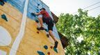Man in red t shirt and shorts climbing up Go Ape Speed Climbing wall at Alexandra Palace.