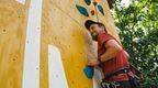 Man in red t shirt and shorts climbing up Go Ape Speed Climbing wall at Alexandra Palace.