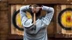 A man in a grey hoodie throwing an axe at a target. 