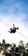 A riding a Go Ape zip wire silhoutted against a blue sky