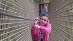 A girl in a pink hoodie on a Go Ape Tibetan Bridge crossing