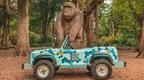 A Go Ape Mini Land Rover parked in front of a wooden gorilla carving in the forest