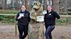 Two women with Go Ape completion certificates next to Go Ape carved sculpture