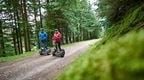 A man and woman riding Forest Segways at Go Ape Whinlatter Forest