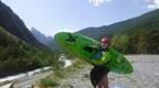 girl in wetsuit with green canoe by lake and mountains