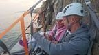 A man and woman in white helmets enjoying a class of champagne on a cliff camping experience