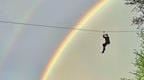Go Ape staff member on a zip wire with a rainbow in the brackground