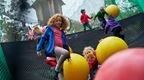 girl with red hair on net adventure climbing walkway with children behind with bouncing balls