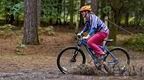 Woman riding a blue bike through the forest splashing through a muddy puddle