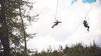 Two people riding a Go Ape dual zip wire