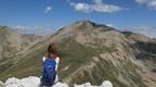 A woman with a blue rucsack sitting ona  rocky ledge looking at a mountain view