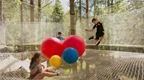A group of children play on a Go Ape Nets Adventure course with giant colourful bouncy balls and the sun shining down on them