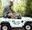 A young boy sitting behind the wheel of a Mini Land Rove in the forest, with his dad sat behind to supervise him on a fun day out