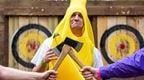 A man wearing a banana outfit for his stag do with his mates holding axes in front of him