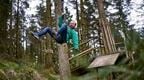 A man wearing a green jacket riding a Go Ape zip wire for a thrilling stag party