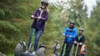 A groupd of people on Go Ape Segways led by a woman ina  purple top
