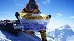 Rupert on top of a mountain with his sponsor flag during his expedition